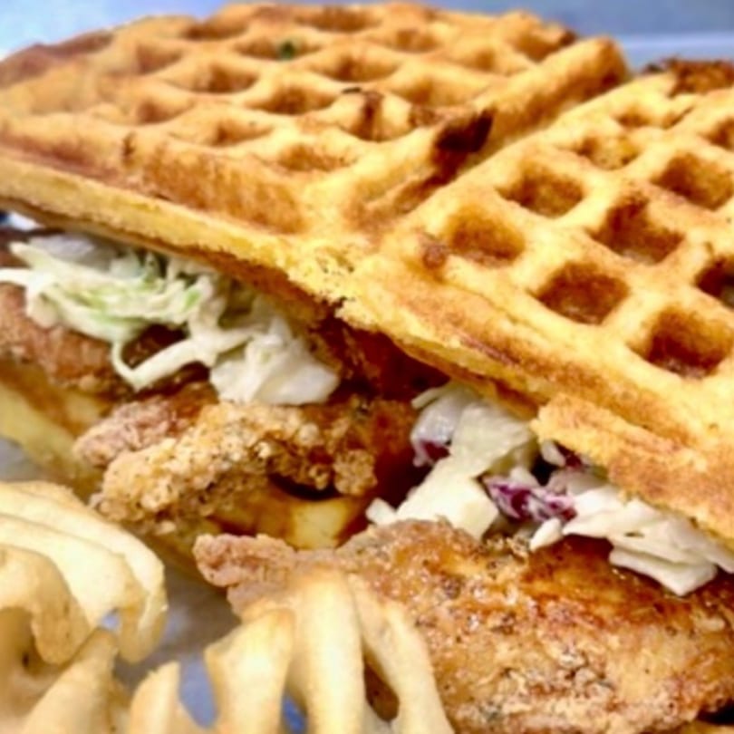 A Munch Munch Waffles & More chicken and waffle sandwich with coleslaw and waffle fries.