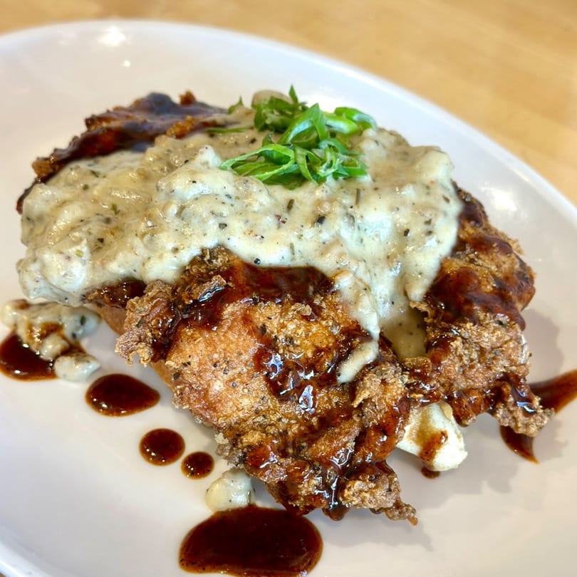 Crispy fried chicken and waffles topped with creamy gravy, garnished with green onions.