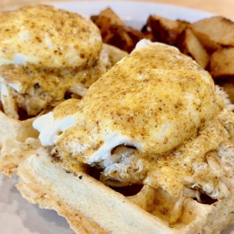 Two crab cake Benedicts on waffles with poached eggs and hollandaise sauce, served with home fries.