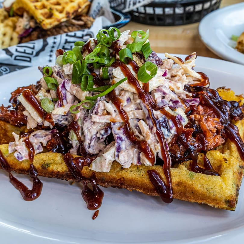 Savory waffle topped with pulled pork, creamy coleslaw, barbecue sauce, and green onions.